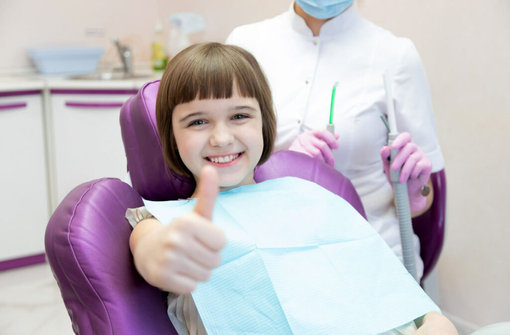 A child smiling with her female dentist, giving a thumbs up while in the dental chair