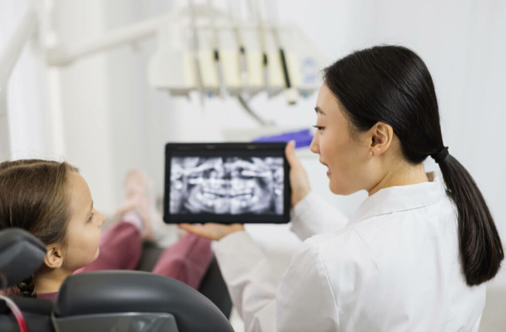 A female dentist explaining a dental procedure to a child while holding a dental X-ray image.