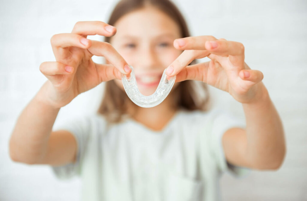 A young patient against a white background smiles as they show off their new Invisalign held between both hands