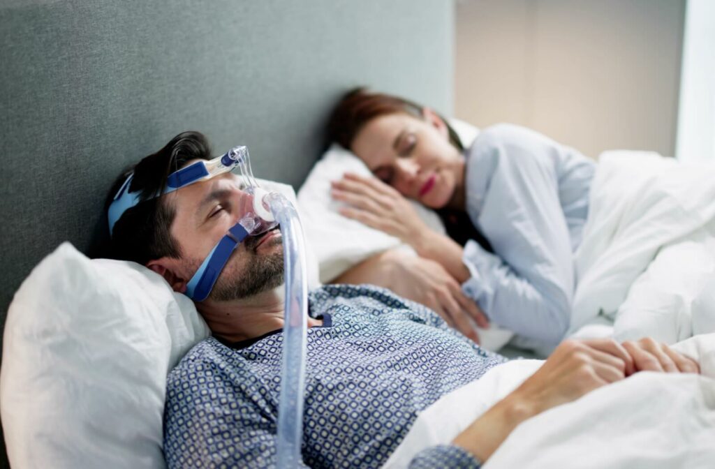 A married couple sleeping peacefully as the husband wears a CPAP machine to prevent snoring from sleep apnea.